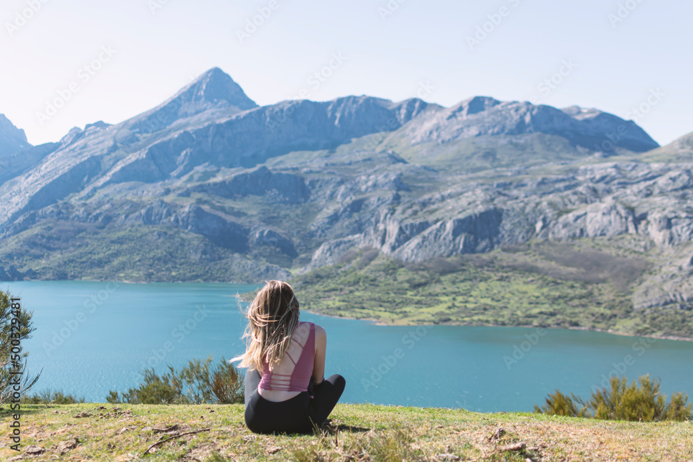 Chica joven relajada y sentada en el cesped observando la montaña en modo zen