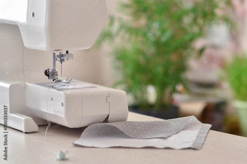 A white sewing machine stands on the table next to the fabric. Atelier and seamstress