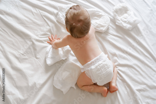 Cute baby in dry soft diaper on white bed at home, top view