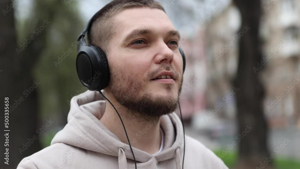 young man puts on headphones while walking in the city park. tourist young man puts on headphones while walking in the city park. tourist