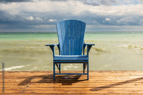 A place to sit and think.  An Adirondack (or Muskoka) chair sits on a simple wooden deck in spring. Shot in Toronto\'s iconic Beaches neighbourhood in early spring.