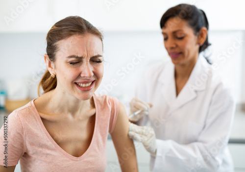 Woman client of medical clinic afraid of syringe while female doctor injecting a vaccine in her arm