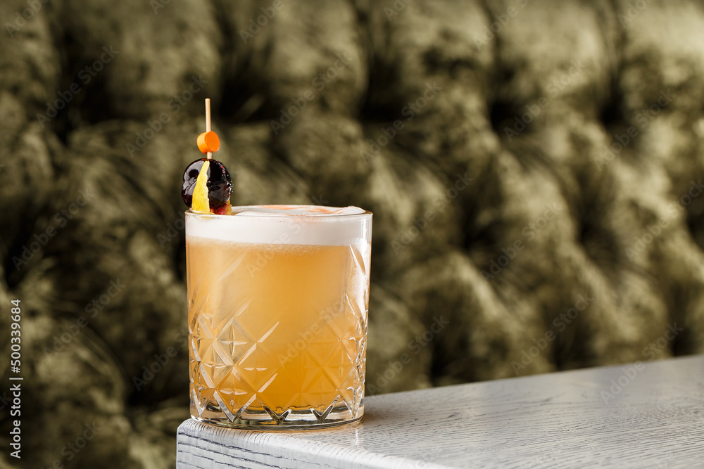 Whiskey Sour alcohol cocktail with orange slice and ice cubes on dark background.