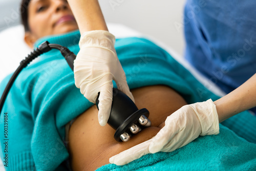 Close up view of young adult woman belly receiving radio frequency abdomen lifting procedure at cosmetology clinic