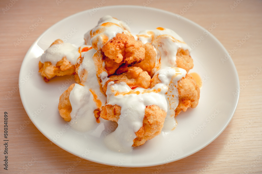 Fried cauliflower sauced with yoghurt and tomato paste in a white plate