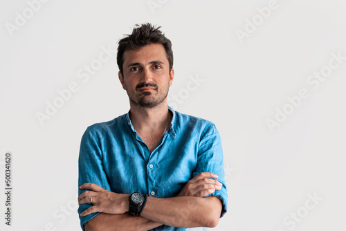 Formal business male portrait. A confident successful casual businessman or manager stands in front of a white background, arms crossed, looking directly at the camera and smiling friendly. High