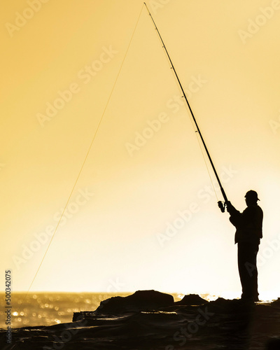 Fisherman on the rocks silhoutted in the early morning sunlight