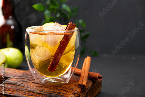 Fotografia A glass of refreshing apple cider with cinnamon and ice on the dark table copy s
