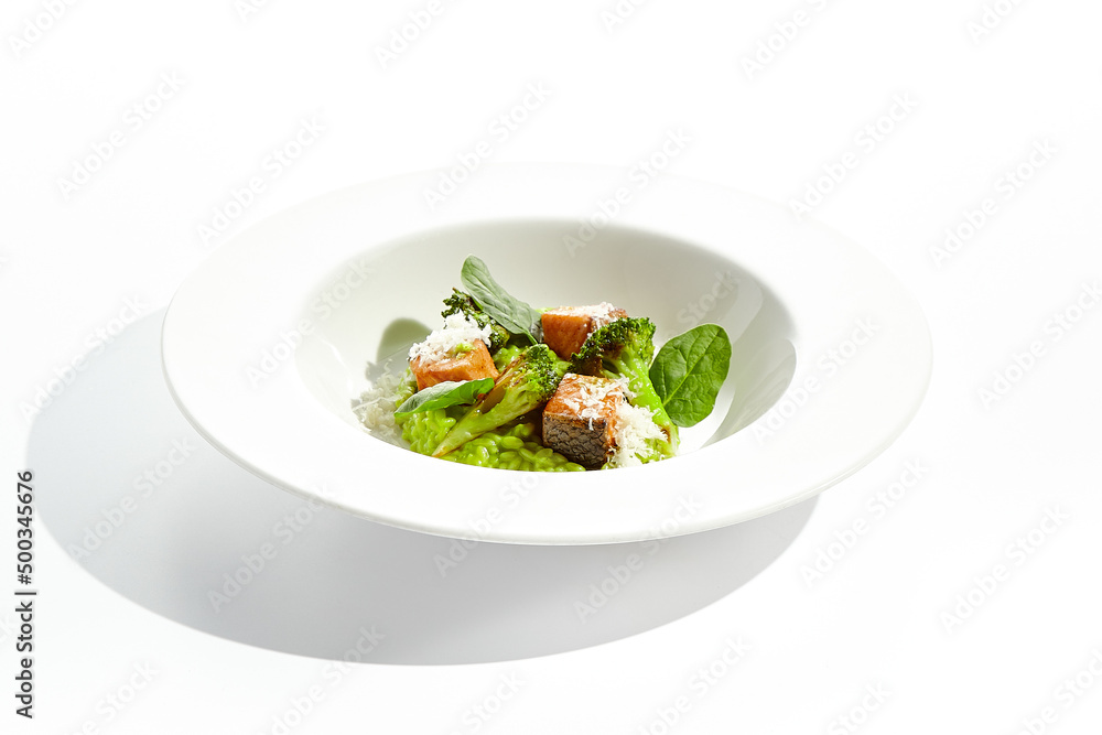 Gourmet food - green risotto with broccoli and salmon on white background. Italian lunch with risotto and sliced grilled salmon. Contemporary dish for restaurant menu. Hard shadow in sunshine day. Gourmet food - green risotto with broccoli and salmon on white background. Italian lunch with risotto and sliced grilled salmon. Contemporary dish for restaurant menu. Hard shadow in sunshine day.