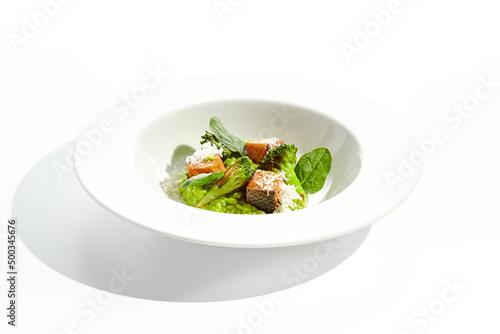 Gourmet food - green risotto with broccoli and salmon on white background. Italian lunch with risotto and sliced grilled salmon. Contemporary dish for restaurant menu. Hard shadow in sunshine day.