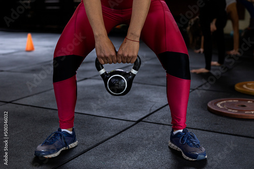 Latin American woman standing with legs open holding kettlebell with both hands during her workout at the gym. Unrecognizable. Healthy Lifestyle Concept.