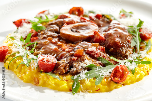 Traditional Italian dish - osso buco with risotto Milanese and cherry tomato and rucola. Ossobuco with saffron rice isolated on white background. Stewed meat on bone with yellow risotto. photo