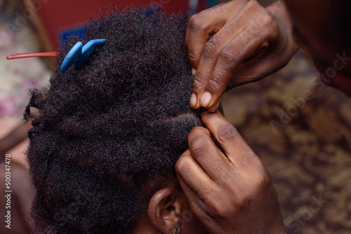 Hands of an african Nigerian hair dresser or stylist making weaving hairstyle for a client in saloon