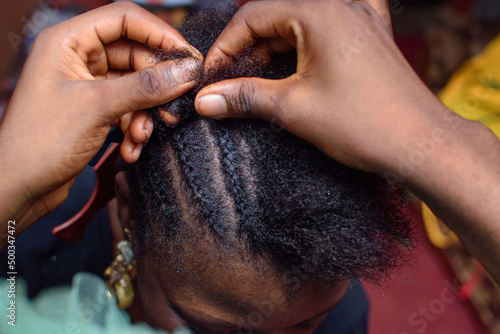 Hands of an african Nigerian hair dresser or stylist making weaving hairstyle for a client in saloon