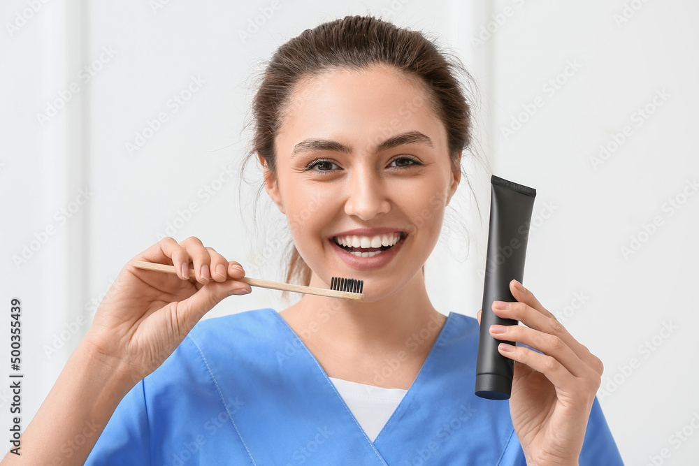 Female dentist with activated charcoal tooth paste and brush on light background Female dentist with activated charcoal tooth paste and brush on light background