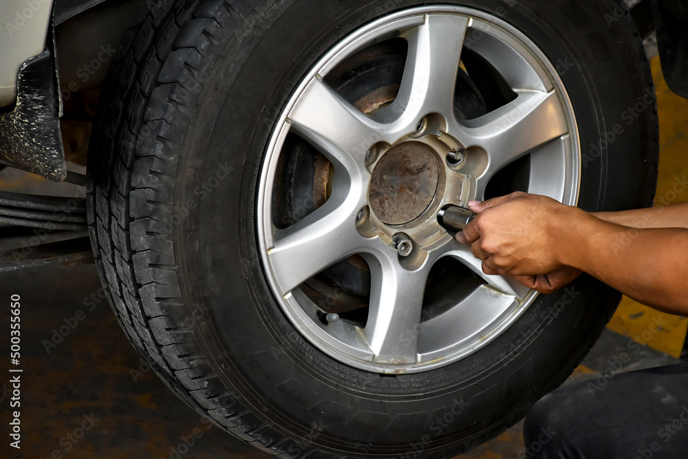 The car attendant  is turning the car wheel back into the car's hub after the tire leak has been repaired, soft and selective focus on wheel, in motion.