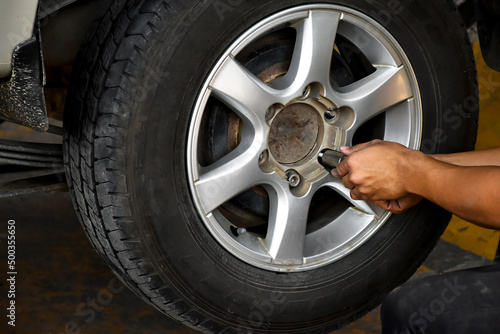The car attendant is turning the car wheel back into the car's hub after the tire leak has been repaired, soft and selective focus on wheel, in motion.