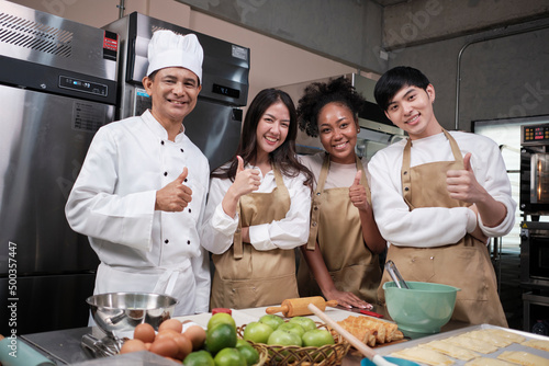 Portrait of professional cooking class people, senior male chef, and young students team looking at camera, cheerful smile and thumb up in kitchen, pastry foods and bakery course for small business.