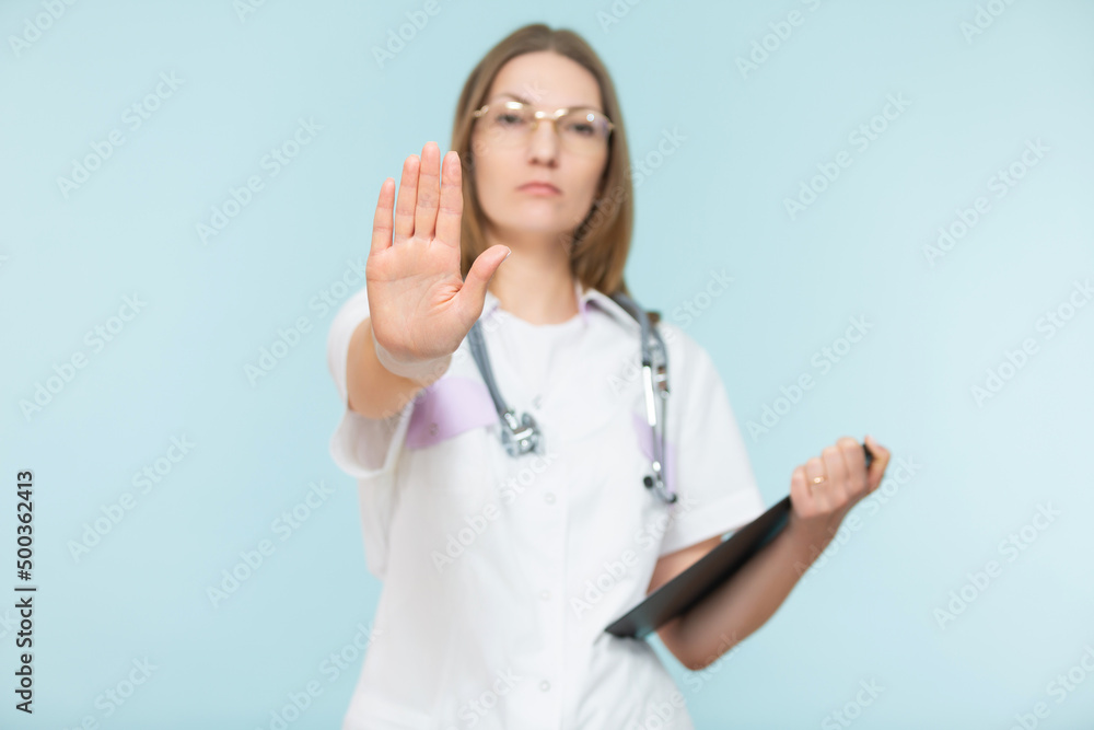 Beautiful woman doctor with a stethoscope and a black tablet, shows a stop sign with her hand, on a blue background. Copy paste. healthcare concept. Let's stop the disease. Beautiful woman doctor with a stethoscope and a black tablet, shows a stop sign with her hand, on a blue background. Copy paste. healthcare concept. Let's stop the disease.