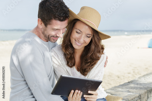 happy couple looking at tablet by the sea © auremar