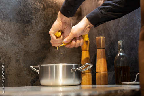 Close-up. A man cooks spaghetti in the kitchen. Breaks the spaghetti into a pot of boiling water.