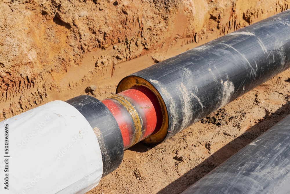 Insulated pipe. Large metal pipes with a plastic sheath laid in a trench. Welding pipes together in a pit at a construction site. Insulated pipe. Large metal pipes with a plastic sheath laid in a trench. Welding pipes together in a pit at a construction site.