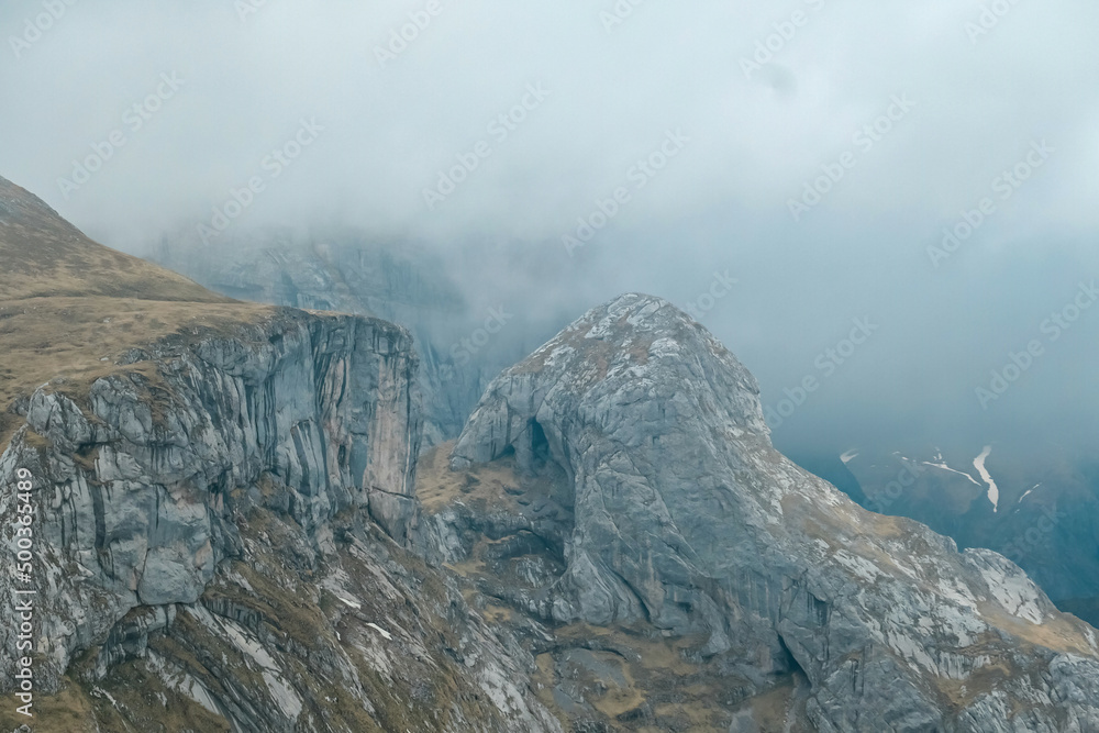 Scenic hiking trail over an alpine meadow in the cloud covered mountain peaks of the Hochschwab Region, Upper Styria, Austria. Rainy spring day in the Alps, Europe. Weather change high altitude. Wind