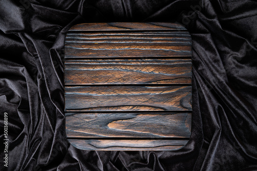 Dark brown square wooden podium for product display on wavy velvet background. Empty textured wooden stand, top view.