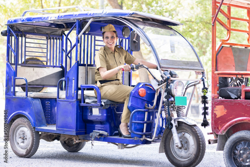 Portrait of happy woman in uniform driving six seater electric rickshaw photo
