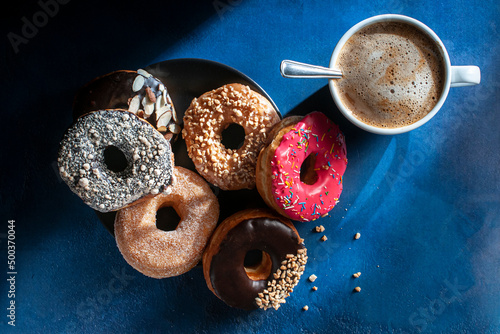 Dark food photography, doughnuts on a  black plate over a blue table with a cup of hot drink coffee chocolate moka. Dark food photography. Flat lay overhead horizontal shot