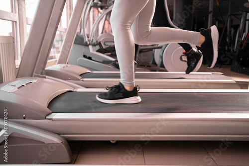 Close-up of sneakers female muscular legs while running on a treadmill in the morning