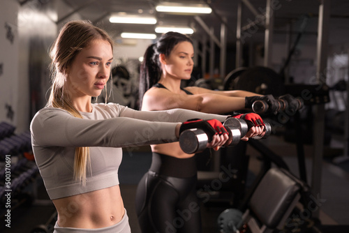 athletic woman goes in for sports with a trainer in the fitness room, lifts dumbbells with her hands.