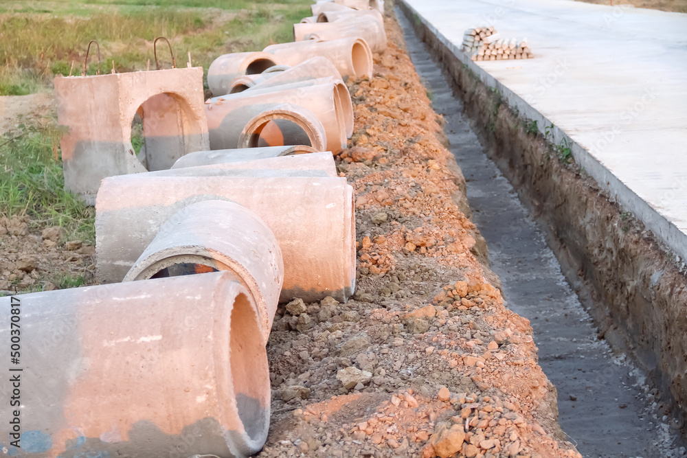 Many big concrete sewage pipes on the ground prepare for underground instalation at road construction site background