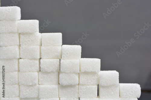 Steps made from sugar cubes. Pile of sugar cubes on a grey shiny surface, sugar pyramid.
