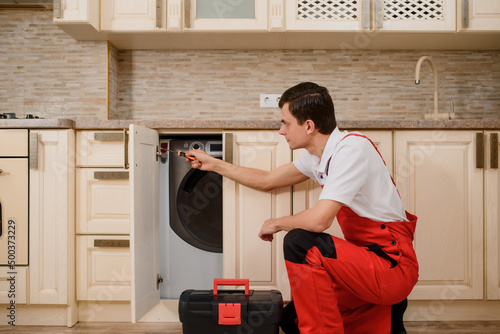 craftsman in red overall finishing assembles furniture in the kitchen.