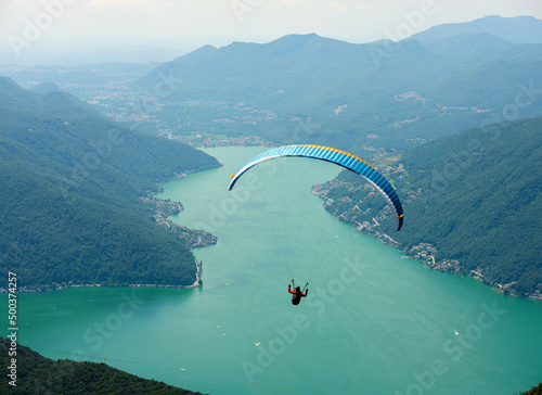 Paraglider that flies from a top of the Intelvi Valley, with a view of the Swiss Alps and Lake Lugano. Concept of lifestyle, freedom and extreme sport adventure.