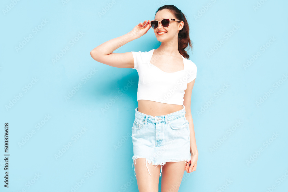 Young beautiful smiling female in trendy summer jeans skirt and top clothes. Sexy carefree woman posing near blue wall in studio. Positive brunette model having fun.Cheerful and happy Young beautiful smiling female in trendy summer jeans skirt and top clothes. Sexy carefree woman posing near blue wall in studio. Positive brunette model having fun.Cheerful and happy