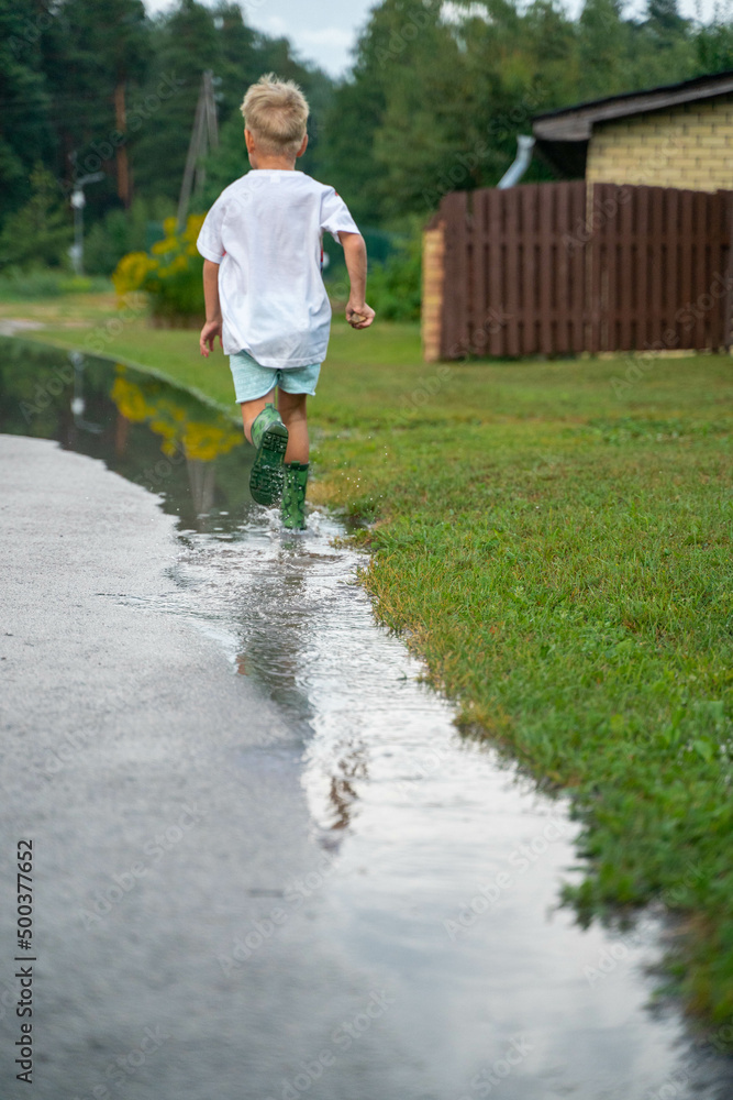 Obraz premium A cheerful child runs through the puddles after the rain on a warm day