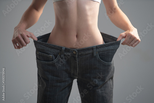 Skinny waist. Slim girl have points at slim waist in big trousers, successful weight loss, isolated on gray background. Successful weight loss, woman with too large jeans after a diet. photo