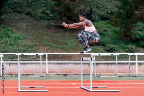 African-American athlete sprinter jumping a hurdle