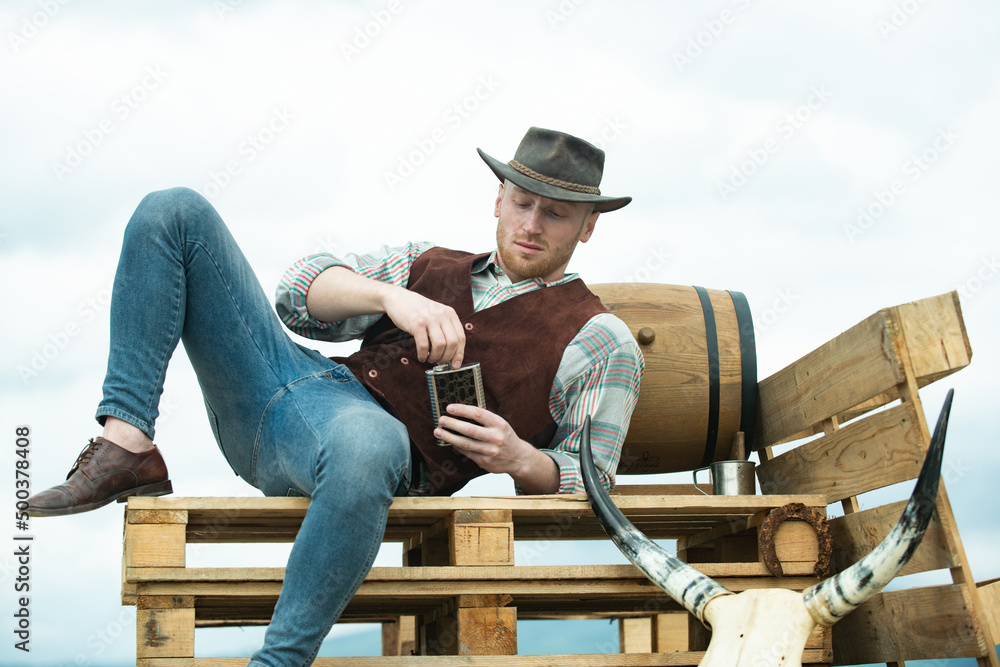 Farmer cowboy wearing hat. Western life. American country male portrait. Farm owner worker in countryside on farm or ranch. Attractive man with whiskey or brandy. Farmer cowboy wearing hat. Western life. American country male portrait. Farm owner worker in countryside on farm or ranch. Attractive man with whiskey or brandy.