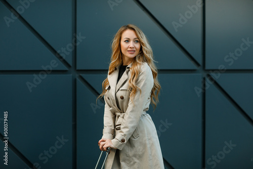 Young beautiful blonde woman with long hair with a suitcase near the airport terminal