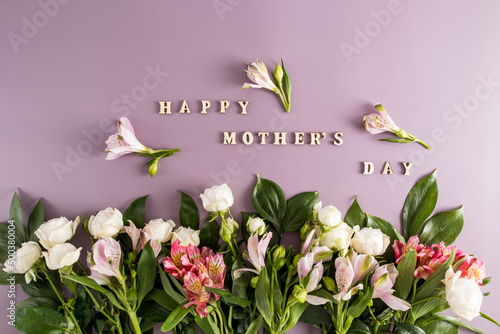 Holiday concept with bouquet of Alstroemeria flowers and roses on pastel pink background. Wooden text happy mothers day. Festive greeting card. photo