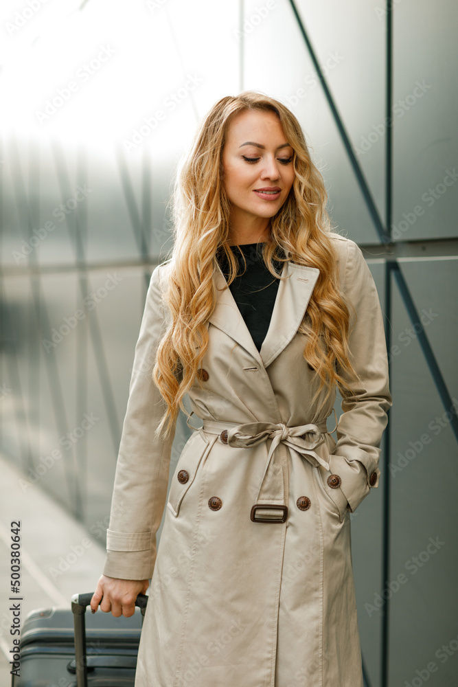 Young beautiful blonde woman with long hair with a suitcase near the airport terminal Young beautiful blonde woman with long hair with a suitcase near the airport terminal
