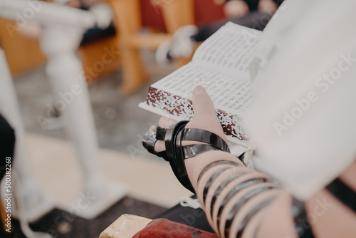 Jewish Man wrapped in tefillin prays. A religious orthodox Jew with arm-tefillin on his left hand, prays. Jewish teenager 13 years old celebrates bar mitzvah reads Jewish bible book photo