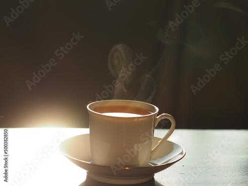 Small Cup Backlight illuminate sun shine close-up steaming hot tea cup, slow motion. Concept Hot ceramic white coffee cup with smoke on old wooden table dark background. Hot Coffee Drink
