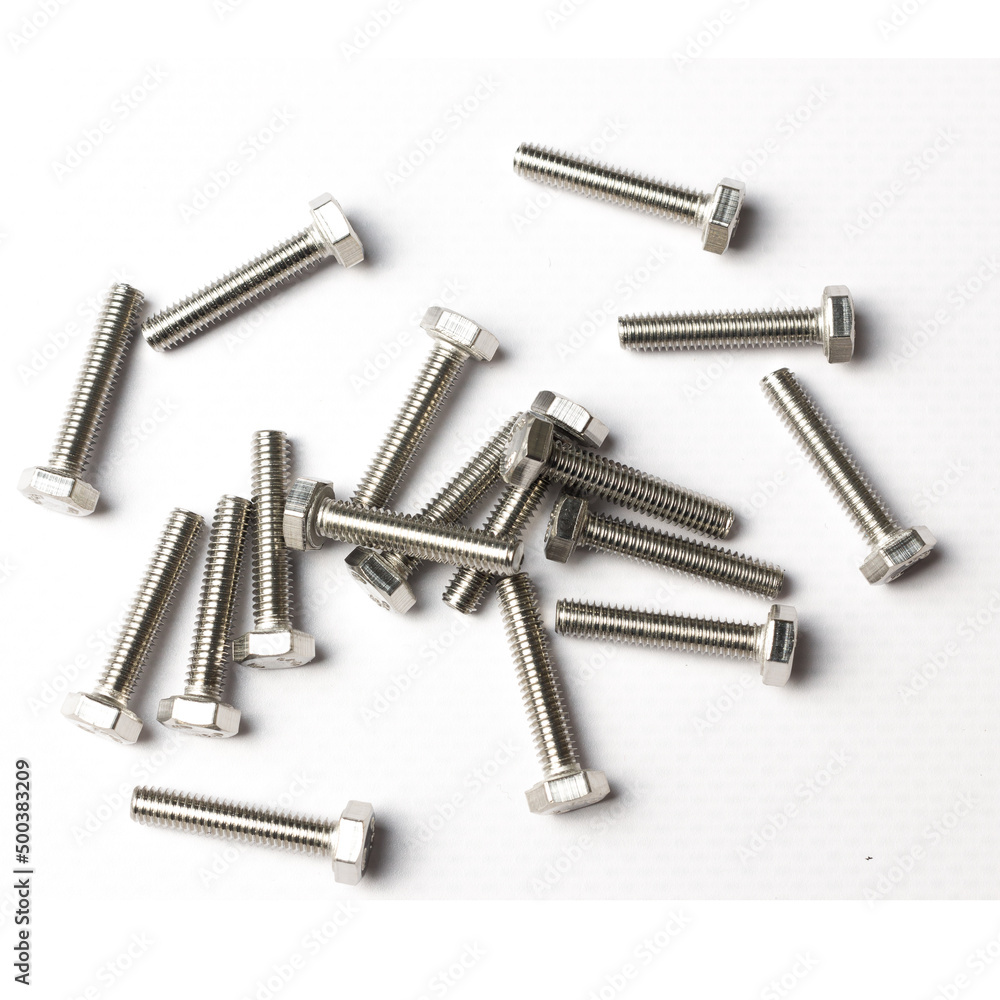 A handful of bolts are scattered across the table with a carving of shiny metal on a white background view from above A handful of bolts are scattered across the table with a carving of shiny metal on a white background view from above