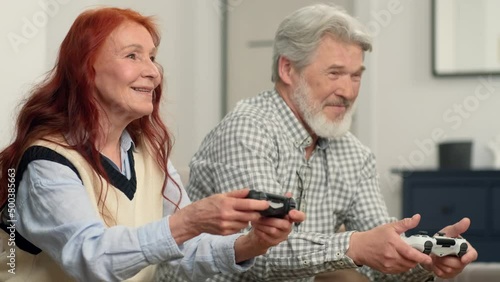 Senior couple 50-60 years old playing football using video game at home sitting on the couch. Game On, Family Meeting, Multi Ethnic Family, Different Generations. photo