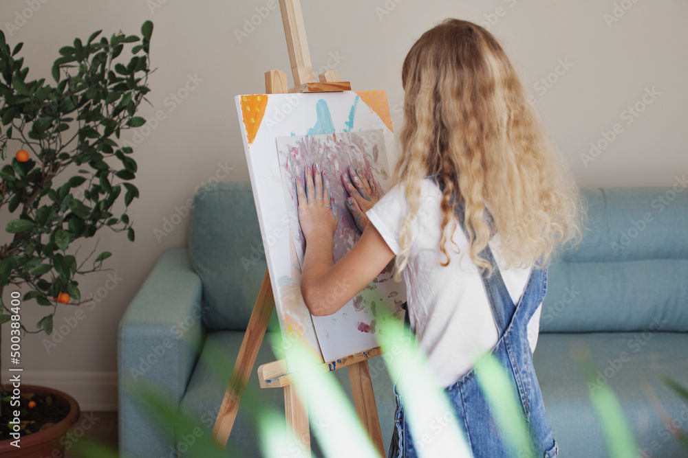 Girl long curly hair painting picture on canvas with her hands. Female model back view Girl long curly hair painting picture on canvas with her hands. Female model back view