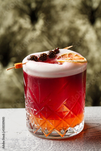 Glass of a New York sour cocktail decorating with small pine cone and orange zest standing on the steel bar counter on the blurred background